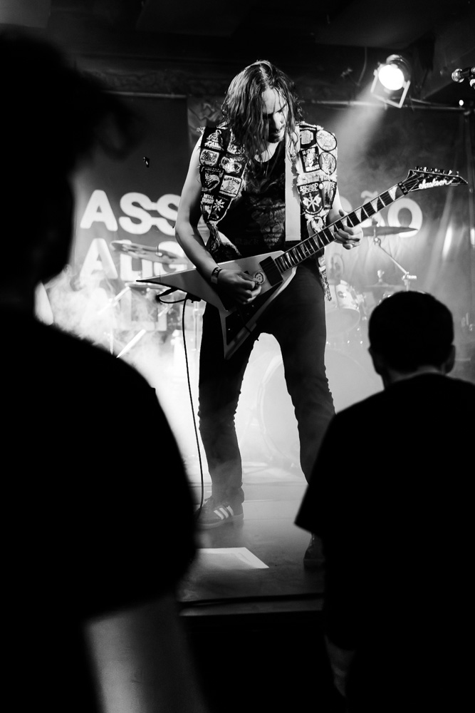 As silhuetas dos espectadores criam uma moldura natural que destaca o guitarrista e acrescenta profundidade à fotografia.